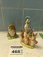 Front view of Timmy Willie, Jemima Puddleduck, and Flopsy Mopsy, Cottontail figurines placed on a countertop with blue tiled background.