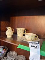 Four-piece set displayed on a wooden shelf including cup and saucer, mug, and small jug with shamrock decals.