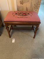 Front view of wooden bench with pink needlepoint floral seat, showing legs and frame