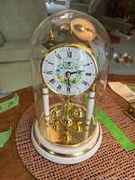 Front view of Birks anniversary clock under glass dome on woven mat.