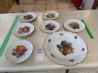 Full set arranged on table showing one large serving platter and six matching plates, each with fruit designs and gold trim.