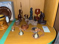 Collection of various items including brass bells on rope, carved wooden figures, a turned wooden wine glass, driftwood candle holder, and decorative medallion.