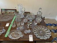 Overall view of all crystal and glass items displayed on table including decanter, plates, jugs, bowls, glasses, and shakers.