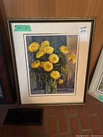 Framed painting showing yellow flowers in a vase, measurement label (27x22) visible, seller's tag attached.