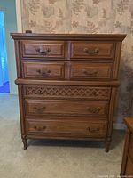 Front view of the brown wood highboy dresser with 5 drawers and decorative carved panel
