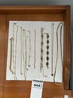 Overview of nine gold-colored chains and bracelets laid out on white pad