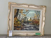 Full front view of framed oil painting showing autumn brook scene, with a large decorative off-white and gold painted frame. Includes MaxSold tag and dimension label.