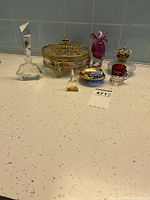 Full view of the lot showing all items: crystal perfume bottle, ornate dresser jar, ruby red bird-shaped perfume bottle, hand-painted bowl, and small decorative cup.
