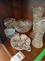Display of four crystal bowls with intricate pinwheel and floral cut patterns on a wooden cabinet shelf.