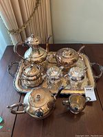 Full view of the silver-plated tea set arranged on a wooden table, showing the tray, two teapots, coffee pot, creamer, sugar bowl, extra teapot and extra creamer.