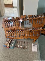 Full view of wooden USA map-shaped rack holding many collectible souvenir spoons, with additional boxed and loose spoons front and bottom.