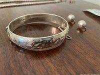 Close-up of sterling silver bracelet with engraved patterns and safety chain, with matching silver screw-back earrings beside it.