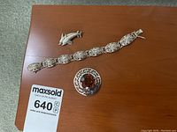 Overview of the lot on a wooden surface including bracelet, round brooch, and dolphin pin.