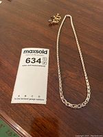 Sterling silver rope chain necklace displayed on wooden surface with gold-tone earrings and auction tag.