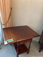 Wood tea cart with drop sides extended, showing dark wood grain and rectangular shape beside curtain and wall