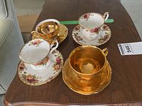 Overhead view of four teacup and saucer sets: three floral bone china and one gold gilt porcelain set on wooden table
