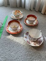 Four vintage teacups and saucers placed on carpet, showing all unique designs and patterns.