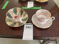 Two vintage teacups with matching saucers on a brown wooden table showing distinct floral and decorative patterns with gold trim.