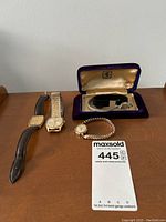 Four watches displayed on a wooden surface, including a purple velvet-lined box holding a ladies watch.