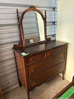 Full view of the antique wooden dresser with tilting mirror detached and resting on top. Dark wood, carved details, and ring drawer pulls visible. Significant surface scratches noted.