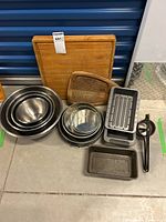 All items of the lot arranged on the floor including wooden cutting boards, mixing bowls, pans, flour sifter, and kitchen tools.