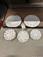 Two larger bone china plates with small red rose patterns on edges, placed on a brown shelf.