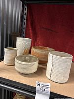 Photo showing five ceramic pottery items on shelf with red backdrop including bowl, vase, cup and two smaller pots.