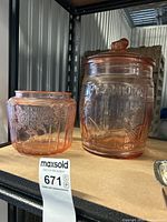 Photo showing two pink glass jars side by side on shelf with Planters Peanuts jar on right and smaller floral jar on left.