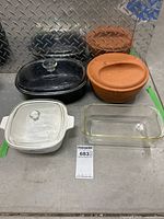 Set of four casserole and baking dishes including Corelle casserole, black casserole, clay crock, and Pyrex rectangular glass dish shown together.