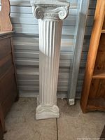 Full view of the white Greek style pillar showing vertical fluted design and scroll details at top and base.