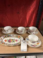 Four two-handle teacups and saucers arranged on a surface with a Dresden plate in front