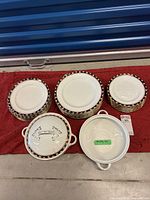 Photo showing three stacks of plates and two white casserole dishes on red fabric. Plates have navy blue and gold patterned border.