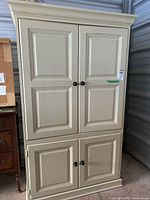 Closed white wooden entertainment unit with double panel doors and round black knobs.