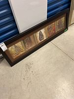 Five panel framed leaf art on a concrete floor against a blue wall with storage units.