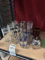 Overview of the lot showing all glassware, coffee mug and stainless steel teapot arranged on shelf against red backdrop.