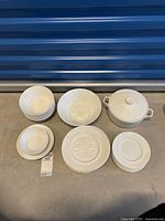 Overall view of the lot showing various plates, bowls, and casserole dish with lid arranged on floor.