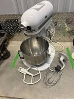 Full view of the white KitchenAid Heavy Duty stand mixer with stainless steel bowl and attachments on a concrete surface.