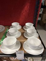 Photo showing all six white Limoges teacups each paired with a saucer, arranged on a surface.