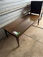 Full view of rectangular wood coffee table with tapered legs and horizontal cutout detail between legs; situated on concrete floor inside metal building.