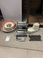 Photo of Himark Kitchen pasta maker with four metal attachments and missing handle alongside five ceramic pasta bowls with Buona San Remo Italia branding.