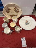 Overview of two plates and six cups on red cloth background, showing overall collection and condition including chips and cracks