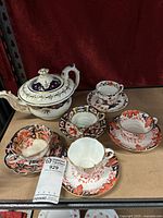 Overview photo showing all four Royal Crown Derby teacups and saucers, one additional teacup and saucer, and the china teapot.