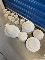 Full set arranged on floor showing cups, saucers, cream and sugar set, plates, and bowls all white with gold trim.