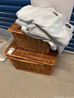 Two stacked wicker baskets with folded grey curtain panels on top, showing baskets' woven construction and size.