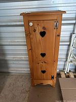Closed wooden cabinet showing front door with three heart cutouts, white knob, and black latch hardware.