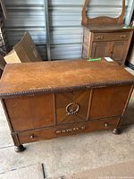 Full view of the wood chest showing front panel, decorative carvings, bottom drawer and feet.
