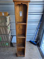 Full view of the narrow wood shelf, showing all four shelves, standing upright in a storage unit with labels visible.