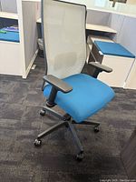 Front view of height adjustable office desk chair showing blue cushioned seat, black adjustable armrests, and white mesh back support with black base and wheels.