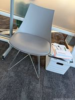 Gray molded office chair with seat cushion and metal wireframe legs, shown in office setting next to a filing box and glass wall.