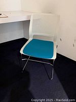 Front view of the white plastic office chair with blue cushion on dark blue carpeting in an office space.
